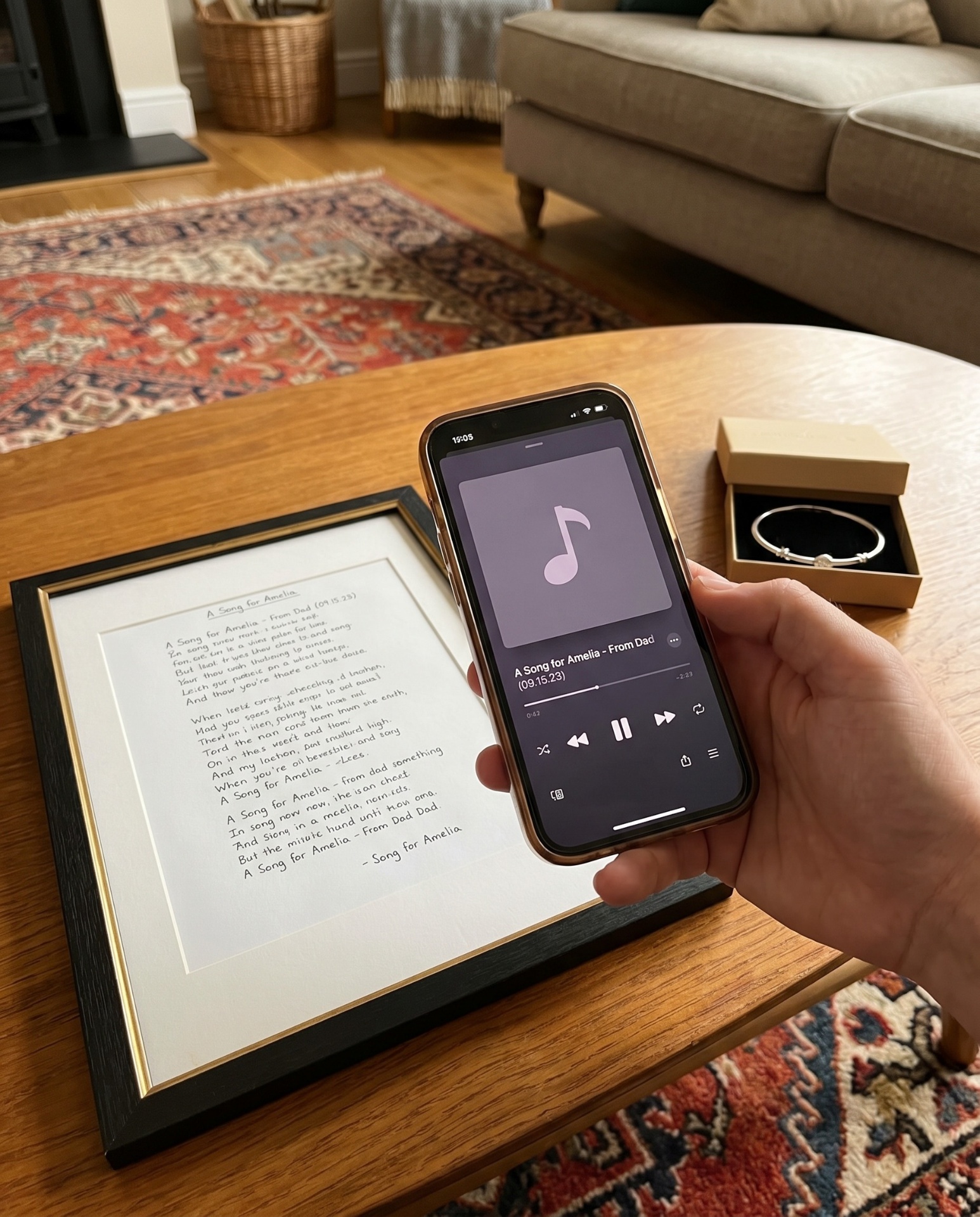 Framed handwritten song lyrics for a daughter beside a phone playing 'A Song for Amelia — From Dad'